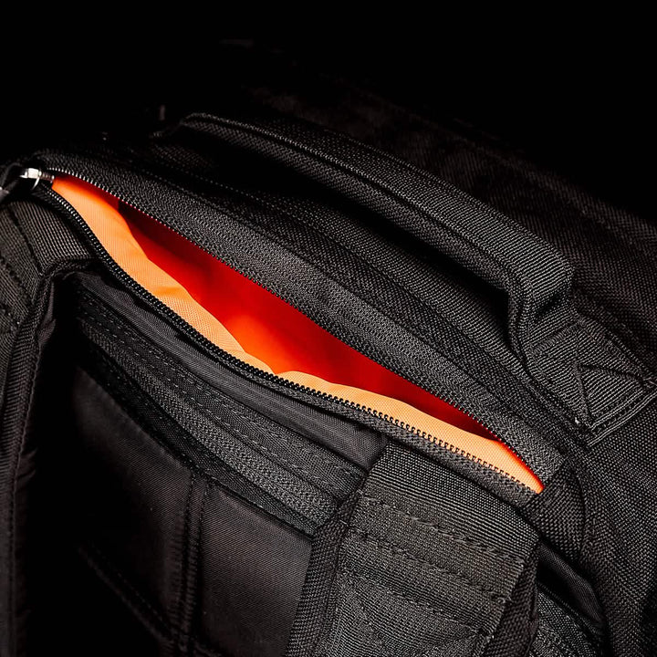 The GORUCK GR1 USA rucksack, in sleek black and made from durable CORDURA, has an open zipper that reveals a vibrant orange interior.