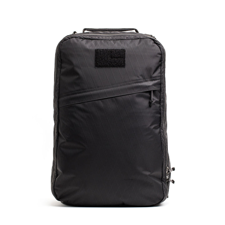 The GORUCK GR1 USA - X-PAC is a black backpack featuring a top handle and AquaGuard zipper on the front pocket, shown against a white background.