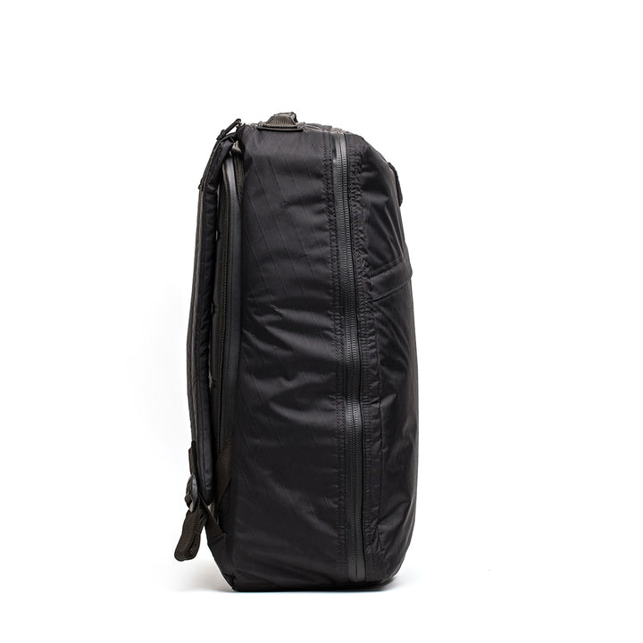 Side view of the sleek black GR1 USA - X-PAC backpack by GORUCK, crafted with X-PAC material and AquaGuard zippers, highlighting its textured design against a white background.