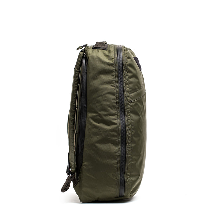 Side view of a green GR1 USA - X-PAC backpack by GORUCK made with X-PAC fabric, displaying AquaGuard zippers on two large waterproof compartments, standing upright against a plain white background.