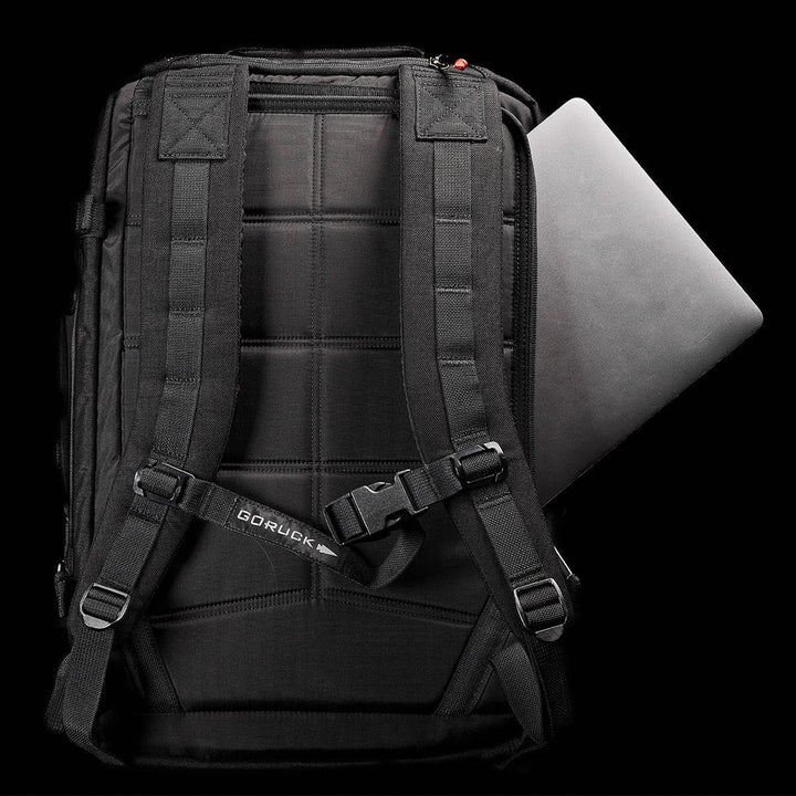 A sleek black GR3 - Cordura backpack by GORUCK, showcasing a laptop partially visible in its side pocket. This carry-on rucksack features padded shoulder straps and water resistance, set against a dark background.