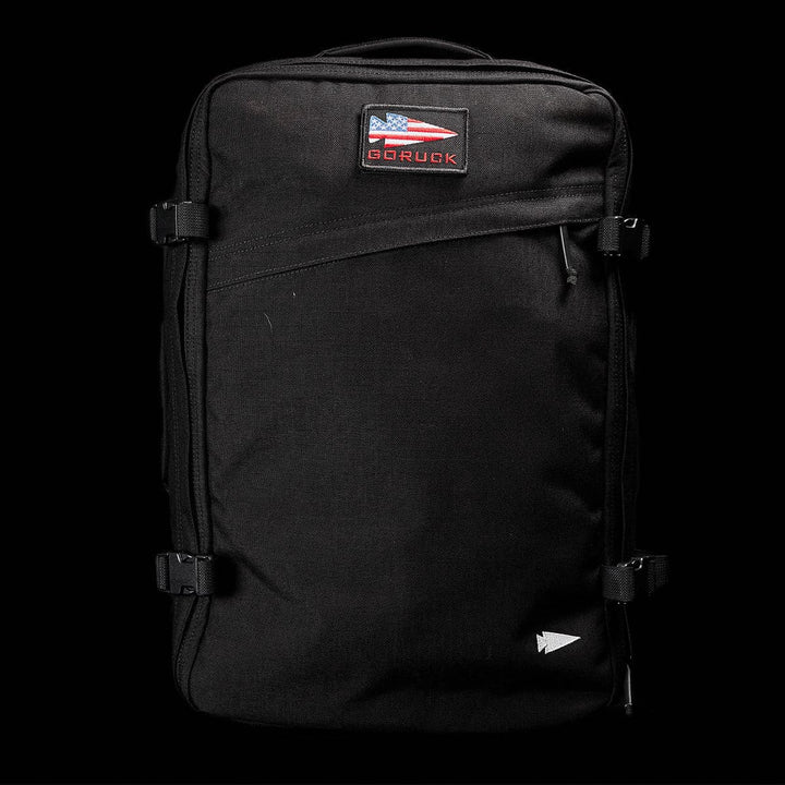 A black GR3 - Cordura carry-on rucksack set against a dark background, showcasing the GORUCK logo with an American flag design on the front. Designed for water resistance, it features side straps and a small triangle logo at the bottom right, capturing the resilient spirit of GORUCK.