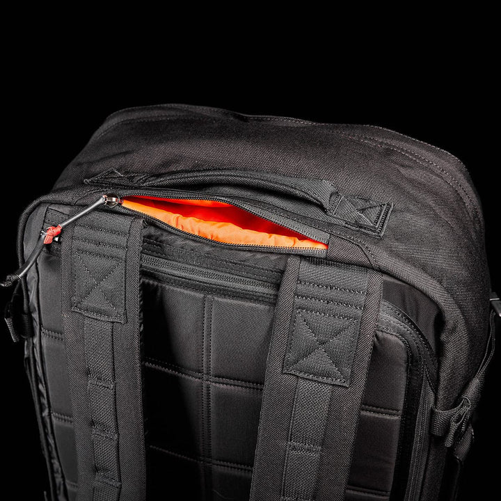 A close-up of the GR3 - Cordura by GORUCK, a black, water-resistant carry-on rucksack, is set against a black background. It features padded straps and a partially open top compartment lined with vibrant orange fabric—perfectly capturing its rugged elegance.