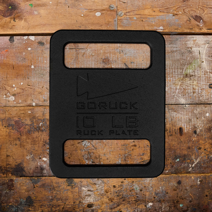 A weathered wooden surface showcases the sleek black 10 LB Ruck Plate by GORUCK, perfect for any dedicated rucker.