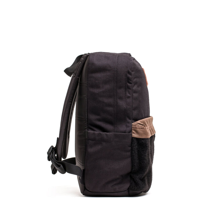 The KR1 2.0 - Kid Ruck by GORUCK is shown in side view, displaying its black design with a brown pocket and adjustable straps. It features reinforced stitching for added durability, all set against a white background.