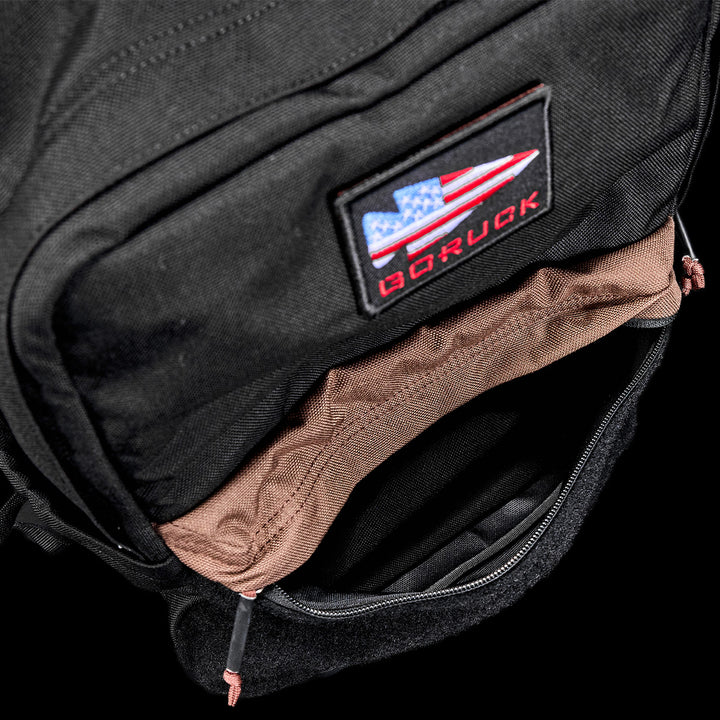 Open black KR1 2.0 - Kid Ruck backpack by GORUCK, showcasing a visible red and blue patch on the front pocket and featuring reinforced stitching for added durability.