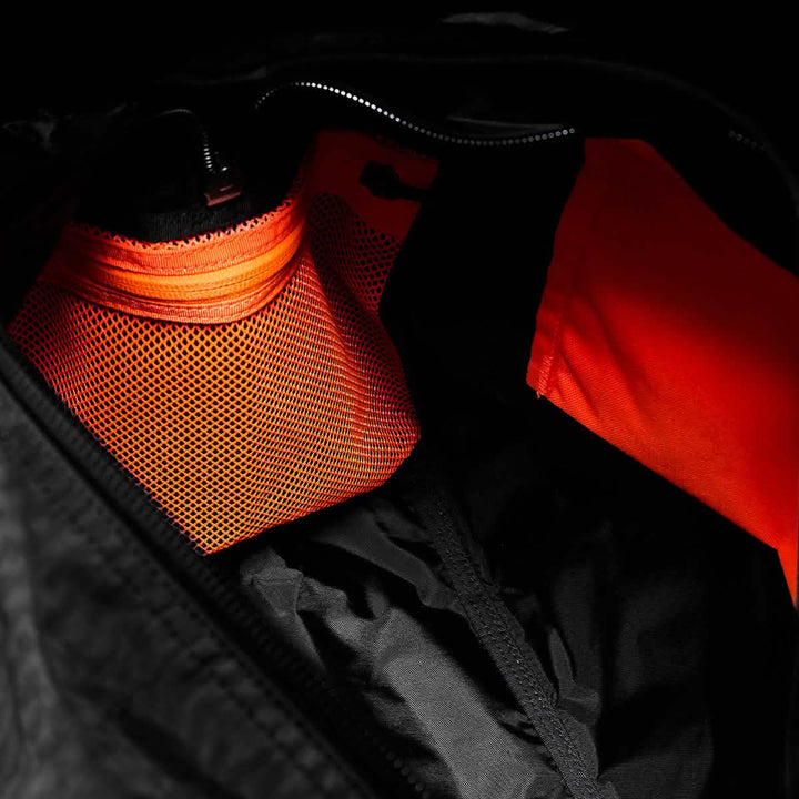 A close-up of a GORUCK Kit Bag - Dyneema interior showcases a vibrant orange mesh pocket paired with a resilient Dyneema section against a dark backdrop. The orange stands out vividly against the surrounding black material, merging durability with style, reminiscent of gear used by Special Forces.