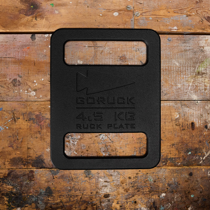 A 4.5 kg Ruck Plates by GORUCK sits on a worn wooden surface with paint splatters, ideal for your Rucker or Ruck Plate Carrier.