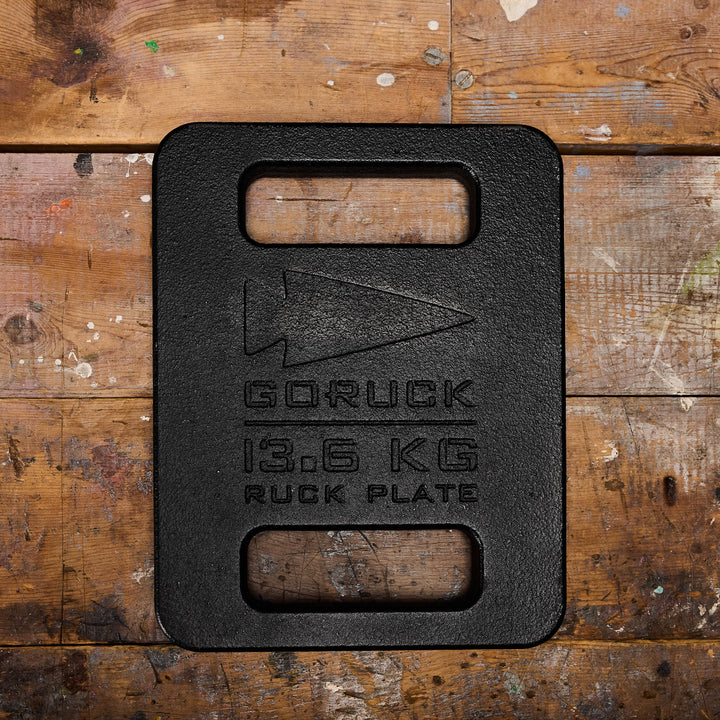 A 13.6 kg black GORUCK Ruck Plate rests on a weathered wooden surface, ready to elevate your Ruck Plate Carrier or Rucker experience.