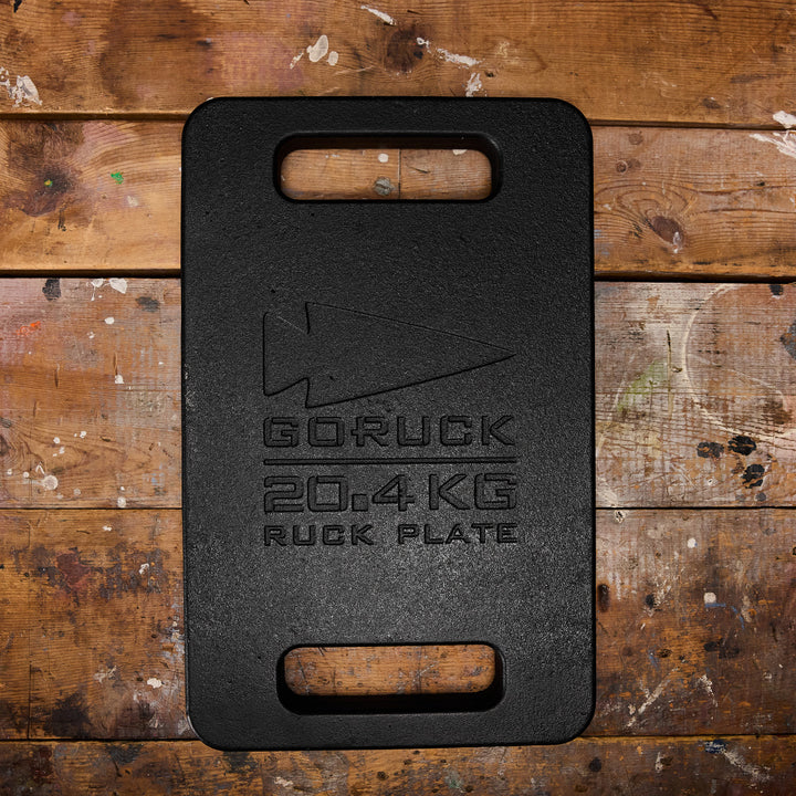 A GORUCK Ruck Plate weighing 20.4 kg sits on a wooden floor speckled with paint, ideal for fitting into your Rucker or Ruck Plate Carrier.