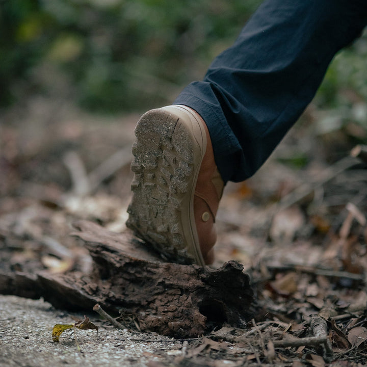 Wearing GORUCK's MACV-2 - Mid Top - Briar + Coyote, featuring an aggressive triple compound outsole, someone confidently steps onto a fallen log along a forest path.