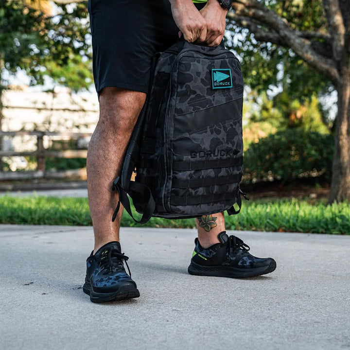 A Rough Runner - Midnight Frogskin + Acid Lime by GORUCK is seen outdoors in the sun, sporting a black camouflage backpack that pairs with versatile road-to-trail outsole sneakers, perfect for spontaneous adventures.