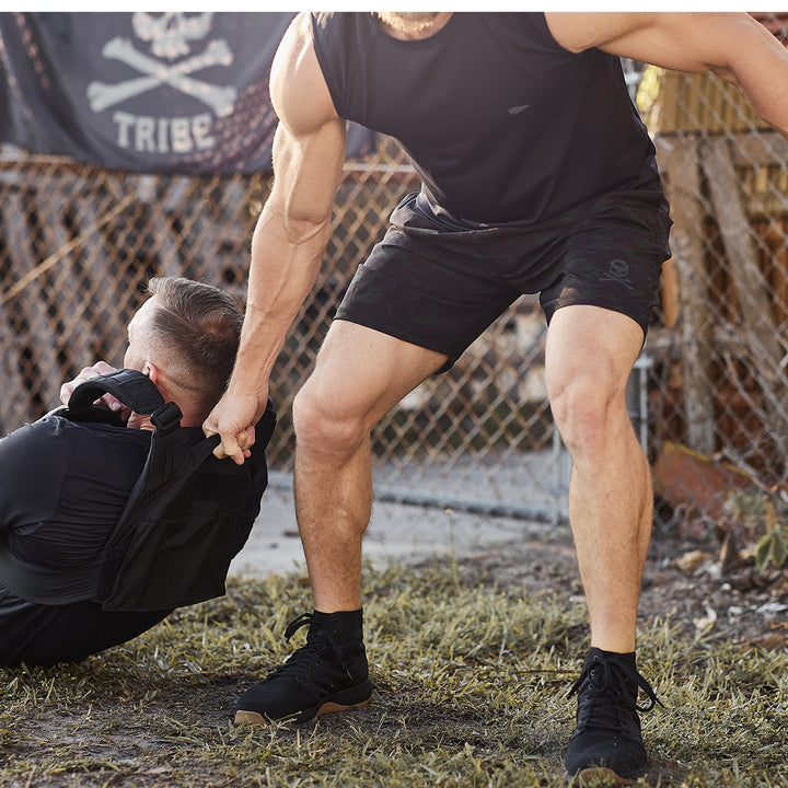 At an outdoor training area, a person drags another by their Ballistic Trainers from GORUCK, crafted with CORDURA® Ballistic Nylon for enhanced durability, 3X support, and maintained stability.