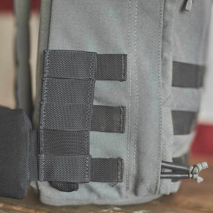 Close-up of a gray GORUCK backpack side, crafted from durable CORDURA fabric, featuring black webbing loops for attaching gear and a GORUCK padded hip belt for enhanced comfort.