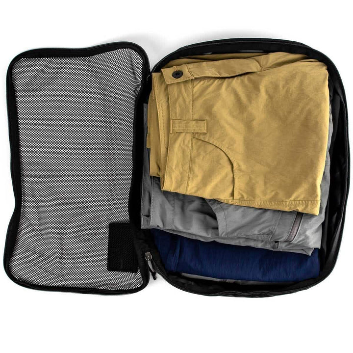 A GORUCK Packing Cube in black, made from ultra-light nylon, showcases neatly folded clothes within—a yellow shirt, a gray garment, and a blue garment—against the plain white backdrop, making it the ultimate travel companion.