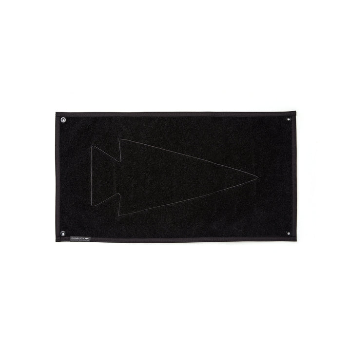 The GORUCK Spearhead Patch Board is a black, rectangular mat made from durable 1000D Cordura and showcases a subtle arrowhead design. It includes grommets at each corner and features an integrated velcro panel for easy customization.