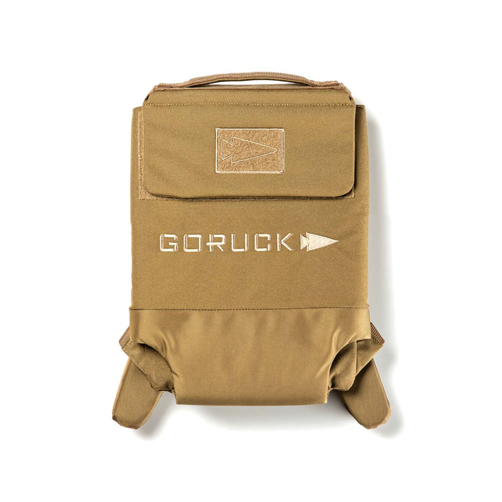 The khaki Ruck Plate Carrier 3.0 by GORUCK, made from durable ballistic nylon, showcases a prominent patch and arrow logo on the front. It is thoughtfully designed for ultimate comfort with ergonomic lumbar support, ideal for any adventure.