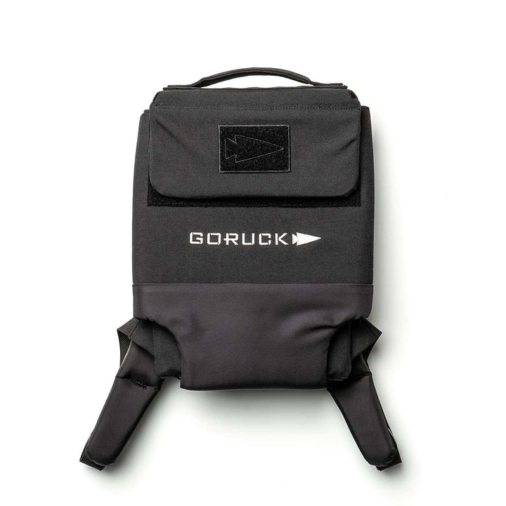 The Ruck Plate Carrier 3.0 by GORUCK, made from sturdy 1000D CORDURA in black, is displayed against a white background. It highlights a distinct logo and arrow design, ergonomic lumbar support, adjustable shoulder straps, and has a flap pocket on top.