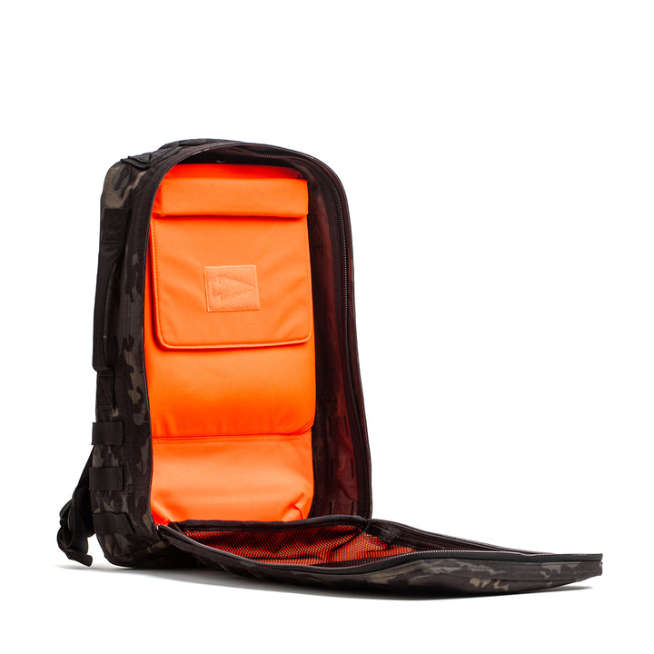 Open the GORUCK Rucker 4.0 backpack with a black camouflage exterior to reveal bright orange interior compartments. It's Ruck Plate compatible for versatile workouts.