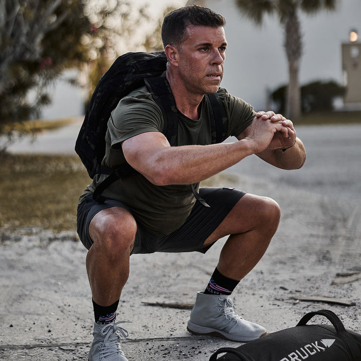 A man doing squats outdoors with the GORUCK Rucker 4.0 securely fastened on his back.