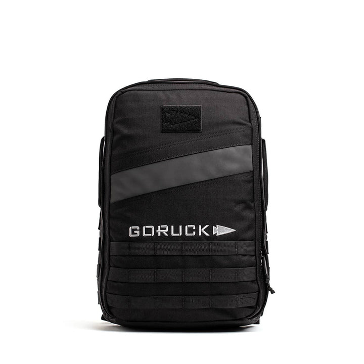 The GORUCK Rucker 4.0, a black rucksack with a diagonal black stripe, logo on the front, and bottom MOLLE system, is ideal for fitness enthusiasts who enjoy rucking adventures.