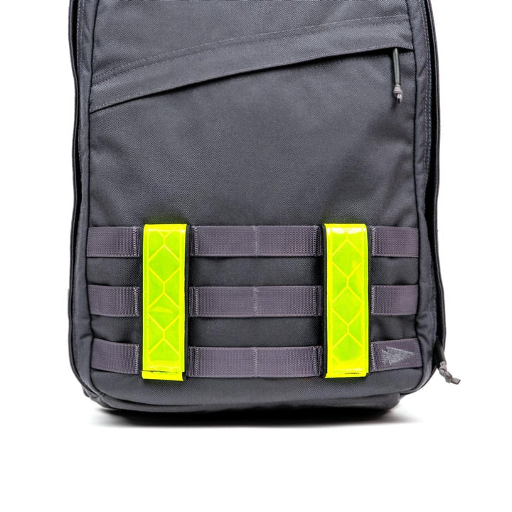 Black backpack with gray straps and two GORUCK Reflective Ruck Bands in bright yellow on the front, ensuring nighttime visibility.