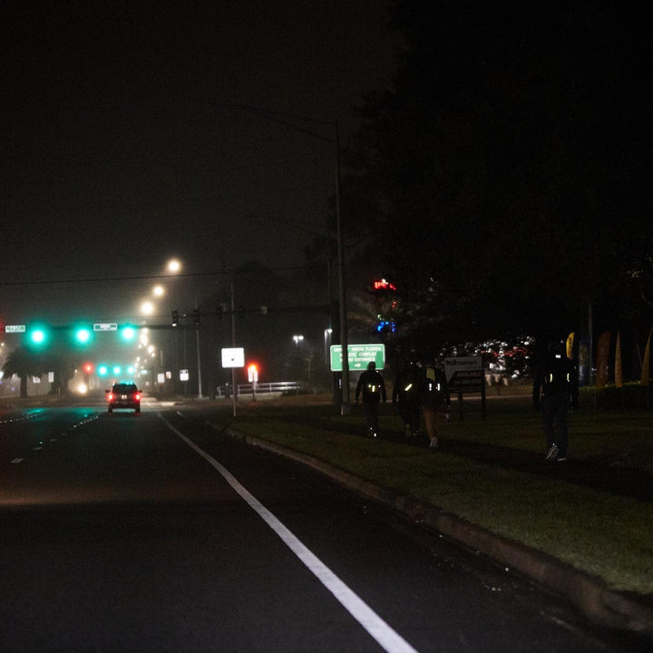 Individuals strolling along a poorly lit sidewalk by the road at night gain improved nighttime visibility, courtesy of GORUCK's Reflective Ruck Bands.