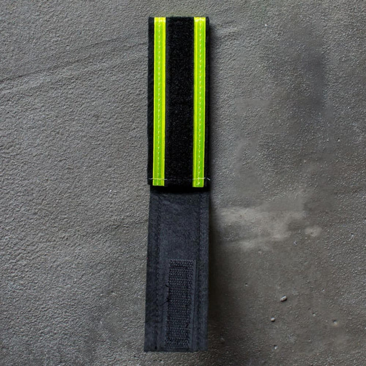 A Reflective Ruck Band from GORUCK, featuring a striking combination of black and neon yellow, sits on a gray surface, making it perfect for nighttime visibility. This versatile accessory is ideal for any situation requiring enhanced safety.