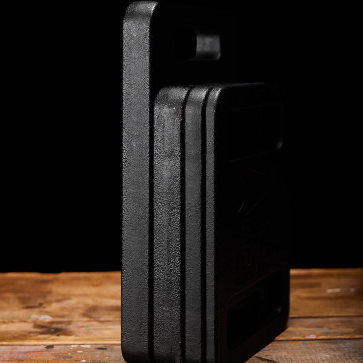 GORUCK Ruck Plates are stacked upright on a wooden surface against a dark background, highlighting their durable design perfect for any Rucker workout.