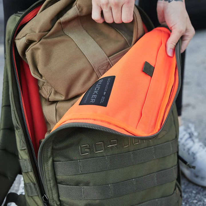 Opening a GORUCK Rucker 4.0 reveals a bright orange interior against its olive green exterior, ideal for rucking adventures.