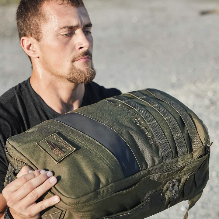 A determined man hoists a GORUCK Rucker 4.0 outdoors, focused and sweaty as he embraces the challenge of rucking.