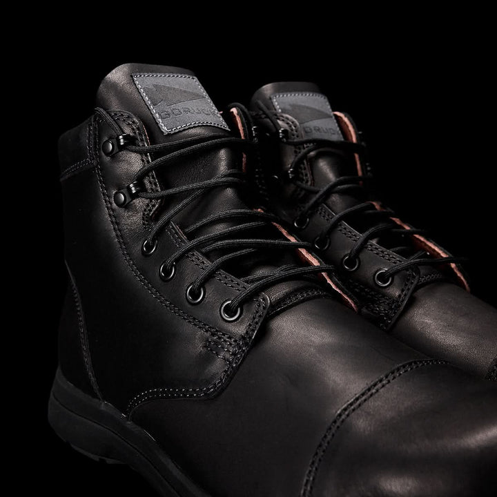 The MACV-1 Traveler by GORUCK are black leather boots highlighted by visible stitching and silver eyelets with matching black laces, set against a dark background. Their design, inspired by airborne jump boots, features a rugged style and an all-terrain outsole, making them perfect for both casual and outdoor adventures.