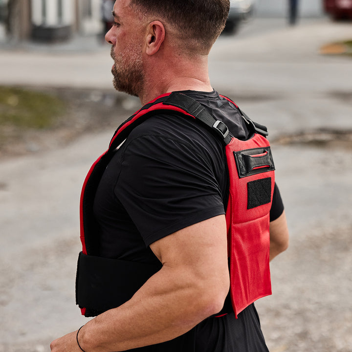 A man wearing a GORUCK Training Weight Vest 2.0 in black is walking outdoors on a street.