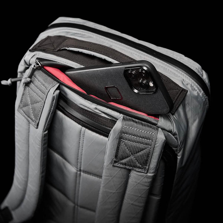 The GORUCK GR1 USA - X-PAC backpack boasts a gray quilted design with AquaGuard zippers, and a phone peeks from its top pocket.