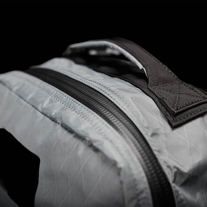 A close-up of the GORUCK GR1 USA - X-PAC bag, made with light gray fabric and enhanced by a durable black AquaGuard zipper and handle, set against a dark background.