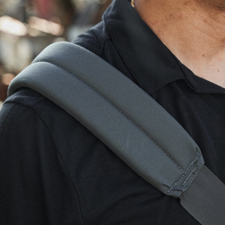 Close-up of a person wearing a black shirt with a padded gray strap from the GORUCK Kit Bag over their shoulder. The focus is on the textured fabric of the strap, and the background is blurred, highlighting its travel-ready appeal.