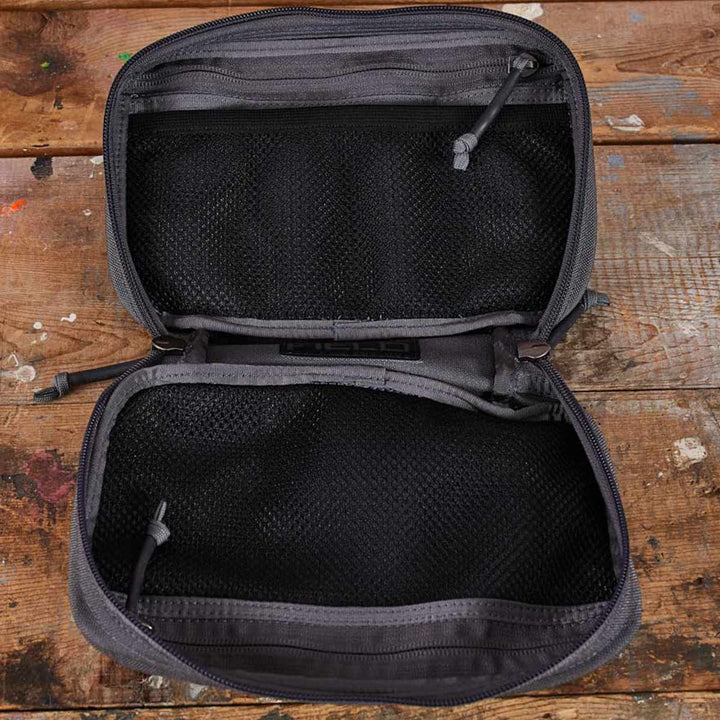 The GR1 Field Pocket by GORUCK, in an open gray design ideal for use as a dopp kit or electronics organizer, features mesh pockets neatly arranged on a wooden surface.