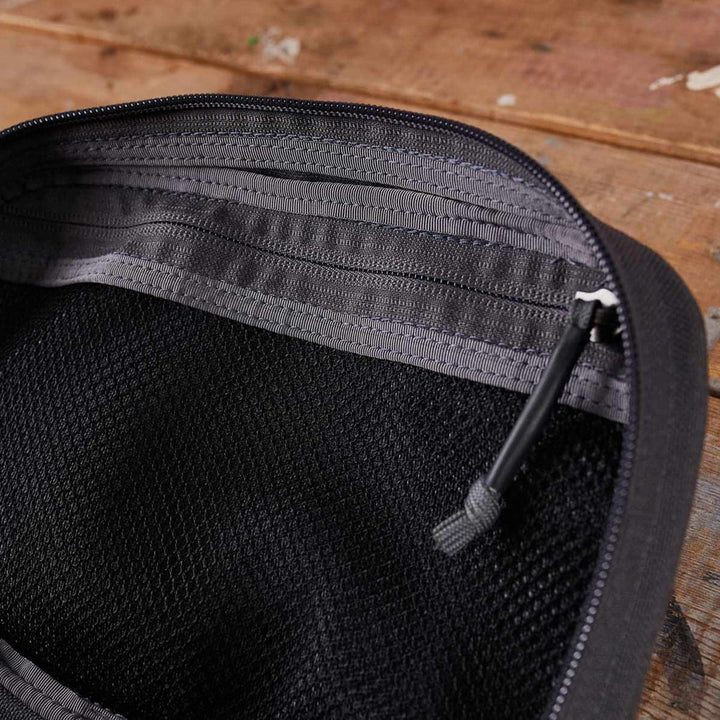 An up-close view showcases the GR1 Field Pocket by GORUCK, an ideal electronics organizer in a sleek black mesh design, elegantly resting on a wooden surface.