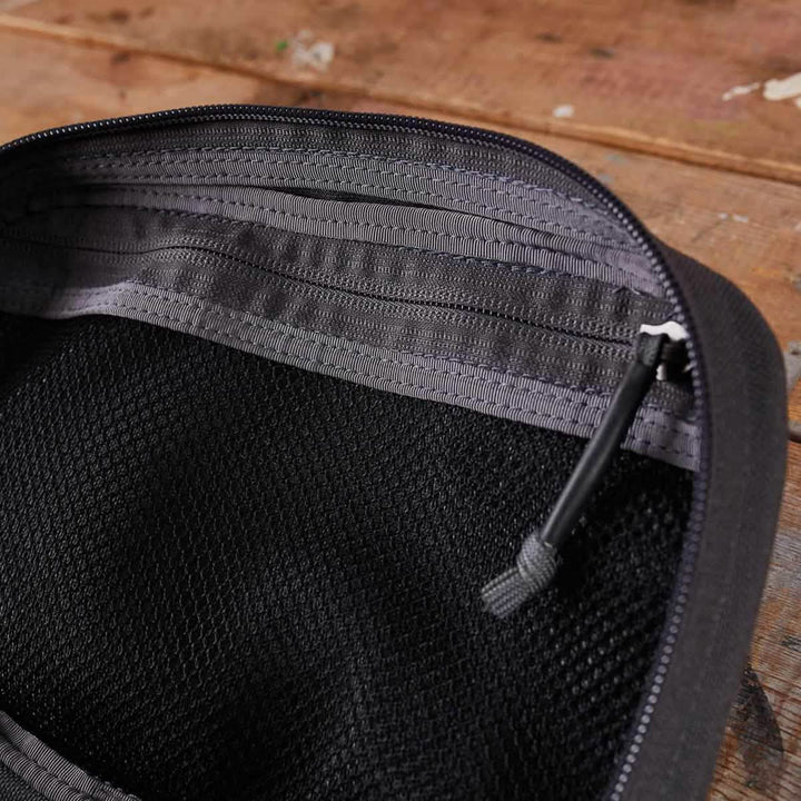 Close-up of an open Armor Grey zippered pouch on a wooden surface, crafted by GORUCK, showing the interior and zipper pull.