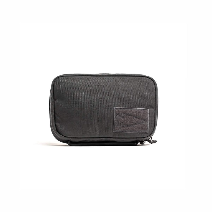 A compact rectangular pouch in black, crafted from durable Cordura by GORUCK, featuring a zipper and adorned with a gray patch showcasing an abstract design on the front. Known as the GR1 Field Pocket - Armor Grey, this product serves as an ideal electronics organizer and is elegantly centered against a plain white background.