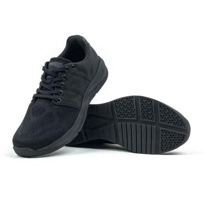 The Ballistic Trainers - Blackout + Black by GORUCK are shown with one shoe upright and the other on its side, highlighting the sole pattern and 3X Support™ technology for enhanced stability. Ideal for functional fitness enthusiasts looking for dependable footwear.