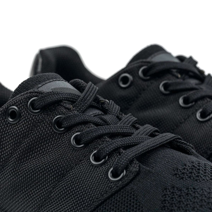 Close-up of the GORUCK Ballistic Trainers - Blackout + Black, showcasing black lace-up sneakers with 3X Support™, textured fabric, and metal eyelets; ideal for functional fitness.