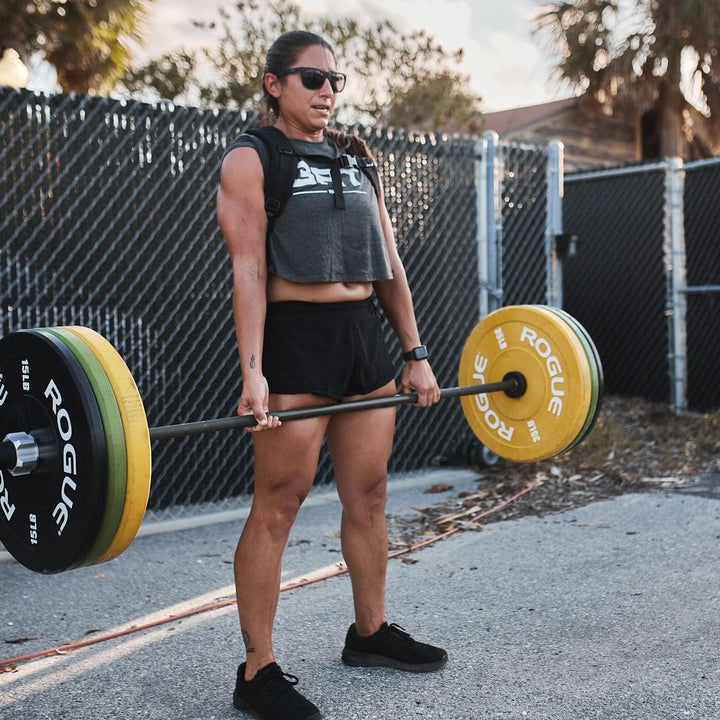 Clad in GORUCK's Ballistic Trainers - Blackout + Black, a person outdoors deadlifts a barbell with yellow and black weights, demonstrating their dedication to functional fitness.