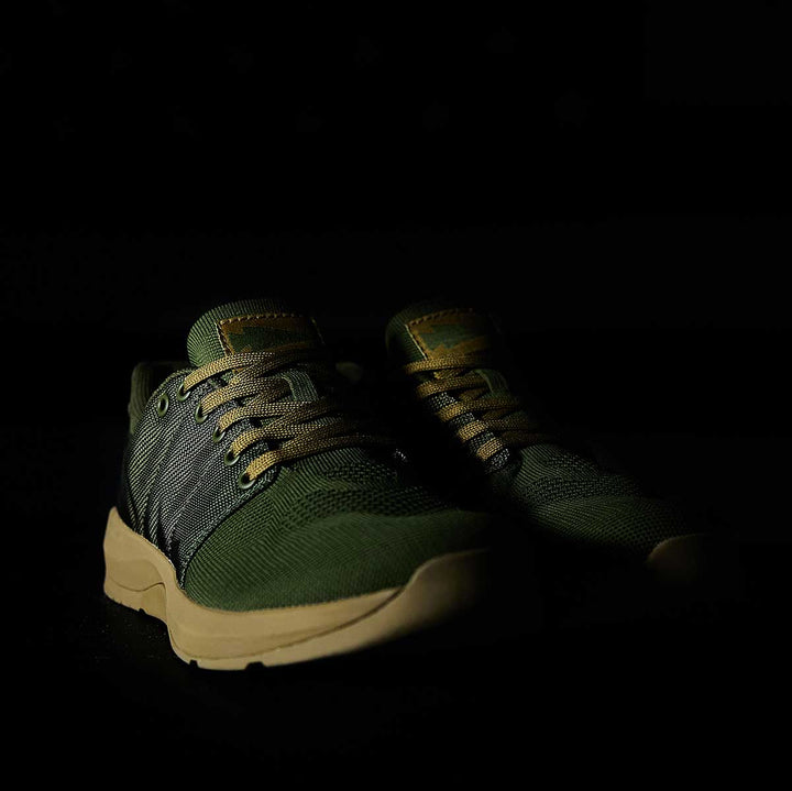 The GORUCK Ballistic Trainers - Green + Gum are athletic shoes made with durable CORDURA® Ballistic Nylon, featuring beige soles and laces for optimal 3X Stability during functional fitness activities, set against a dark background.