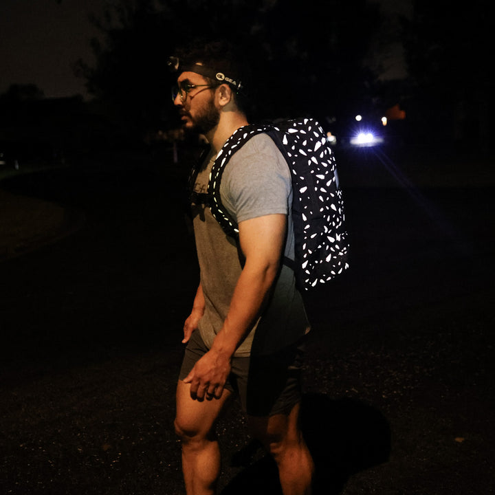 A person carrying a reflective Rucker 4.0 backpack by GORUCK and using a headlamp, lighting up the dark street as they ruck at night.