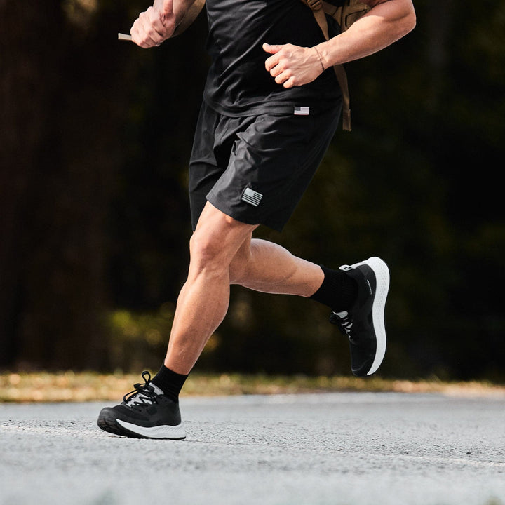 A person jogging on a paved road wearing Men's Rough Runner - Black + White from GORUCK. The background is blurred with greenery.