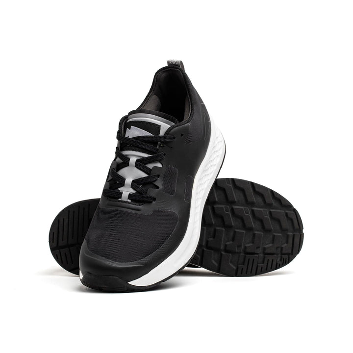 Men's Rough Runner shoes from GORUCK in black and white are showcased on a white background. One shoe is upright with its laces visible, while the other emphasizes the tread pattern and lightweight running design, featuring a Gradient Density EVA Midsole for optimal comfort.