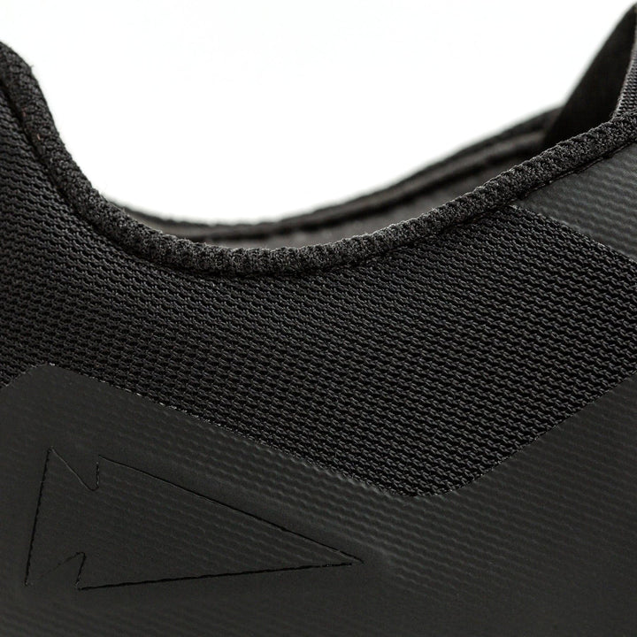 Close-up of the Men's Rough Runner - Black + White by GORUCK showcases a textured fabric and sleek design. The side features an embossed arrow-like pattern, with detailed craftsmanship that offers a modern and minimalist appearance. Perfect for Rough Runner events, this lightweight running shoe ensures comfort and style.