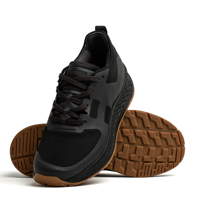 Introducing the Rough Runner - Black + Gum by GORUCK: a black athletic shoe with a textured brown sole. One shoe is displayed on and leaning against another, showcasing its GRADIENT DENSITY™ EVA MIDSOLE that ensures ultimate comfort. These ultra-supportive running shoes feature a versatile road-to-trail outsole, perfect for all your adventurous pursuits.