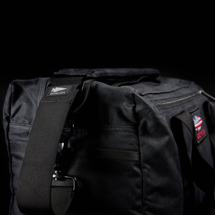 Close-up of a black Kit Bag - Waxed Canvas by GORUCK with a shoulder strap, set against a dark background.